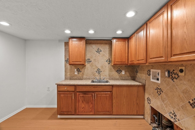 kitchen featuring baseboards, light wood-style flooring, a sink, decorative backsplash, and brown cabinets