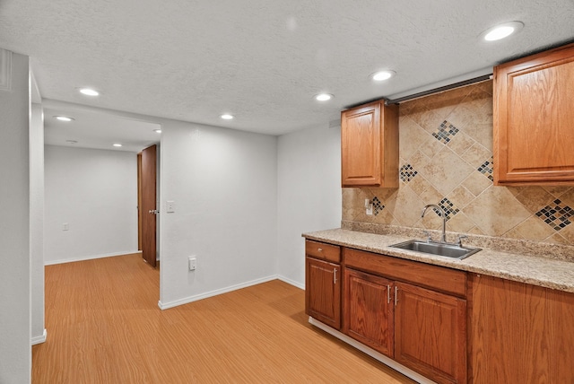 kitchen featuring baseboards, a sink, light wood-style floors, a textured ceiling, and tasteful backsplash