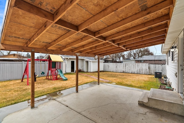 view of patio featuring a storage unit, an outbuilding, a fenced backyard, and a playground