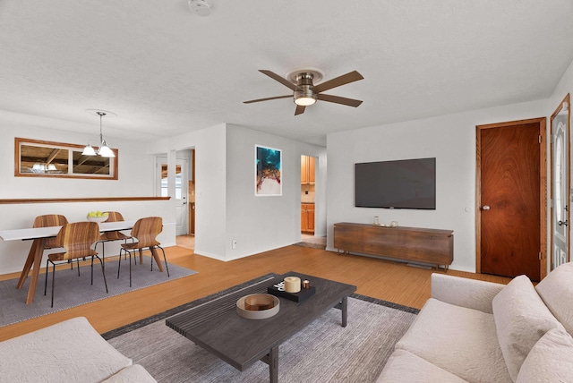 living area featuring ceiling fan, baseboards, a textured ceiling, and wood finished floors