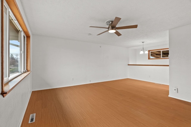 spare room featuring visible vents, ceiling fan with notable chandelier, a textured ceiling, wood finished floors, and baseboards