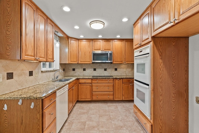 kitchen featuring white appliances, light stone countertops, a sink, brown cabinets, and backsplash