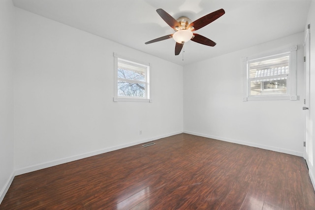 unfurnished room with a ceiling fan, visible vents, dark wood-style floors, and baseboards