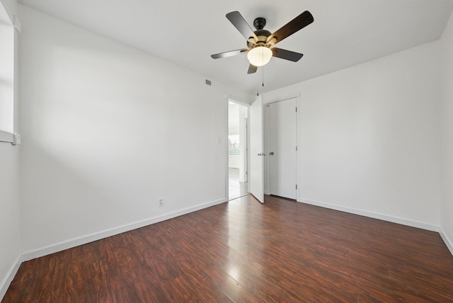 unfurnished room with a ceiling fan, visible vents, dark wood-style floors, and baseboards