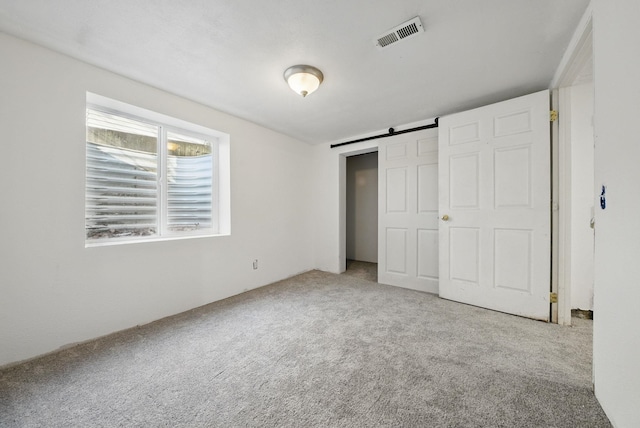 unfurnished bedroom with a barn door, carpet, and visible vents