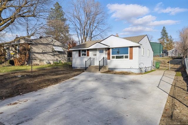 bungalow-style home with concrete driveway, roof with shingles, and fence