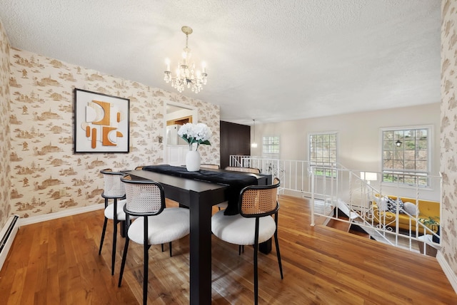 dining area featuring wood finished floors, a textured ceiling, a chandelier, and wallpapered walls