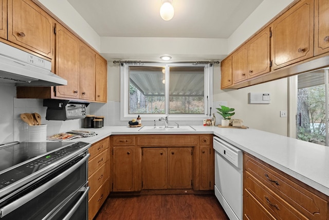 kitchen featuring a sink, under cabinet range hood, white dishwasher, light countertops, and range with two ovens