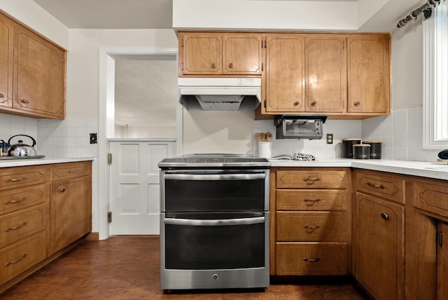 kitchen with light countertops, brown cabinetry, double oven range, and under cabinet range hood