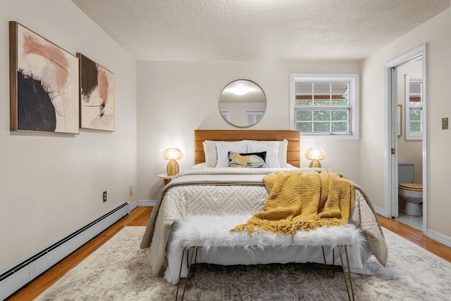 bedroom featuring a textured ceiling, a baseboard heating unit, baseboards, and wood finished floors