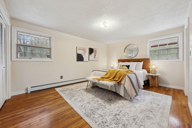 bedroom featuring baseboards, a baseboard radiator, a closet, a textured ceiling, and light wood-type flooring