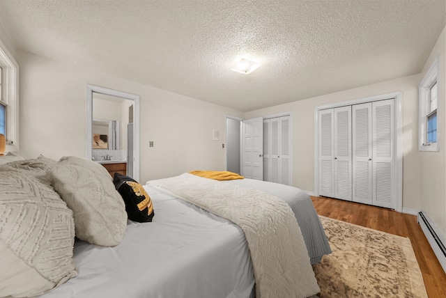 bedroom featuring two closets, a baseboard heating unit, a textured ceiling, wood finished floors, and connected bathroom