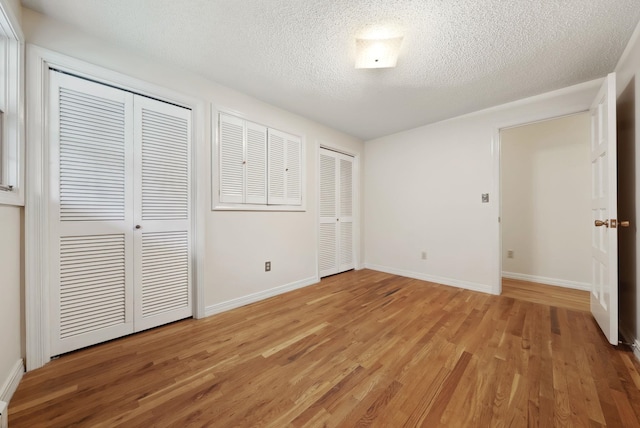 unfurnished bedroom with baseboards, multiple closets, a textured ceiling, and light wood finished floors