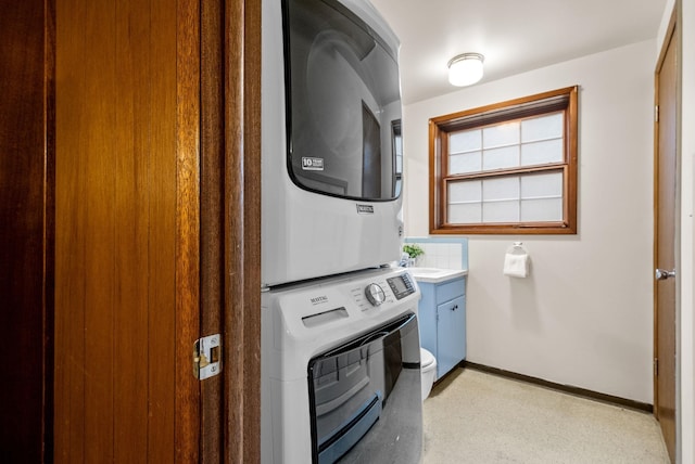 laundry area with baseboards, cabinet space, and stacked washer / dryer