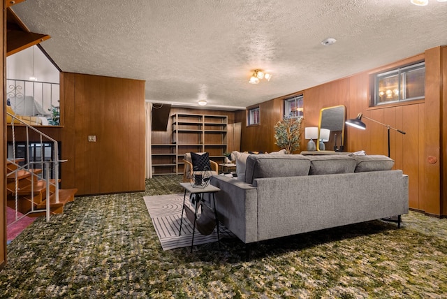 carpeted living area with wooden walls, stairs, and a textured ceiling