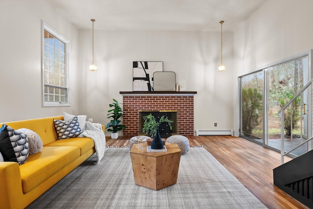 living area with a baseboard heating unit, a high ceiling, wood finished floors, and a fireplace