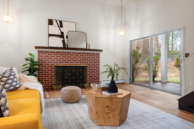 living room featuring a baseboard heating unit, a high ceiling, wood finished floors, and a fireplace