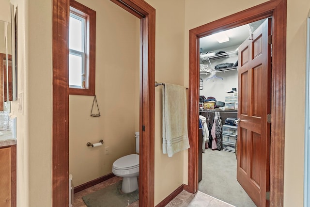 bathroom with toilet, a walk in closet, and baseboards