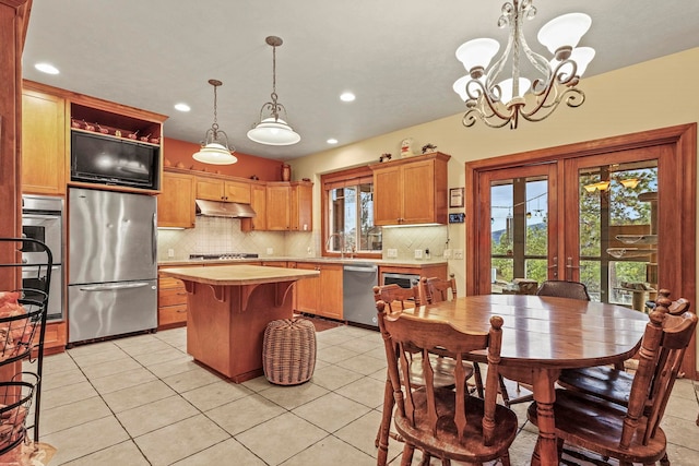 kitchen with a kitchen island, under cabinet range hood, decorative backsplash, an inviting chandelier, and stainless steel appliances