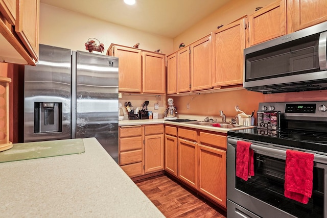 kitchen with wood finished floors, light brown cabinets, a sink, light countertops, and appliances with stainless steel finishes