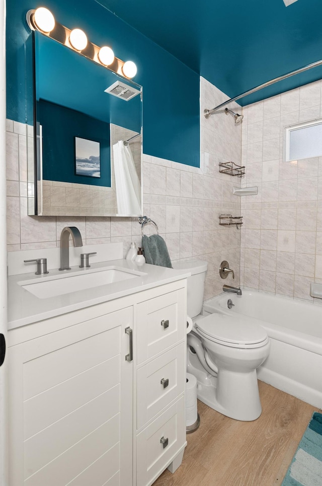 bathroom with toilet, wood finished floors, tile walls, shower / bath combination with curtain, and vanity