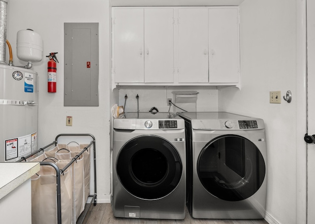 washroom featuring strapped water heater, washing machine and dryer, electric panel, light wood-style flooring, and cabinet space