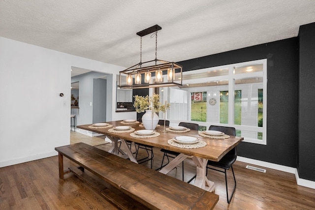 dining space featuring visible vents, a textured ceiling, baseboards, and wood finished floors