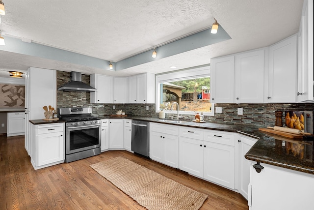 kitchen with light wood-style flooring, a sink, stainless steel appliances, wall chimney range hood, and backsplash