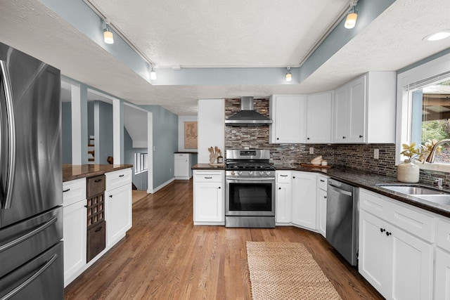 kitchen featuring a sink, appliances with stainless steel finishes, a textured ceiling, dark countertops, and wall chimney range hood