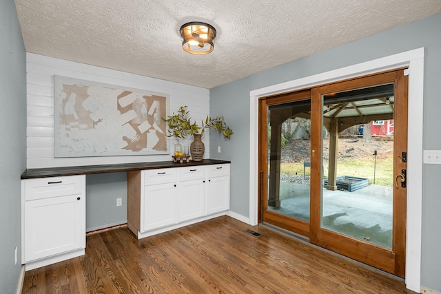 doorway with visible vents, a textured ceiling, and dark wood-style flooring