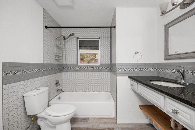 bathroom with toilet, wood finished floors, tile walls, bathing tub / shower combination, and vanity