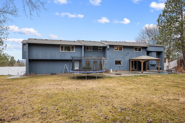 back of house featuring a yard, a fenced backyard, a chimney, a trampoline, and a patio area