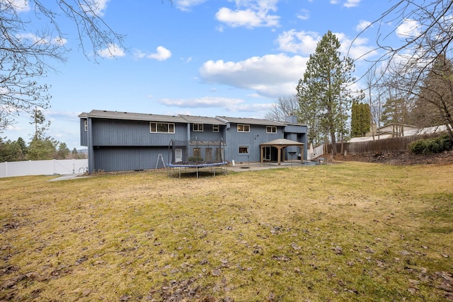 rear view of property with a gazebo, a trampoline, a fenced backyard, and a lawn