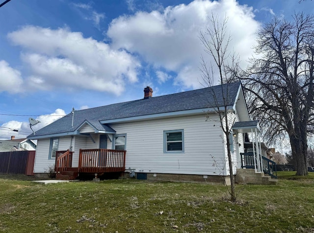 rear view of house featuring a shingled roof, fence, a lawn, a chimney, and a deck