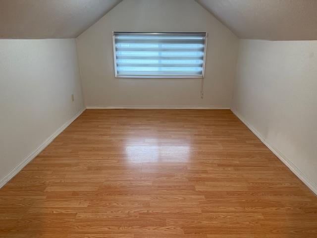 additional living space featuring baseboards, vaulted ceiling, and light wood finished floors