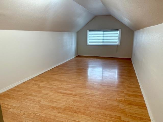 bonus room with baseboards, a textured ceiling, lofted ceiling, and light wood-style floors