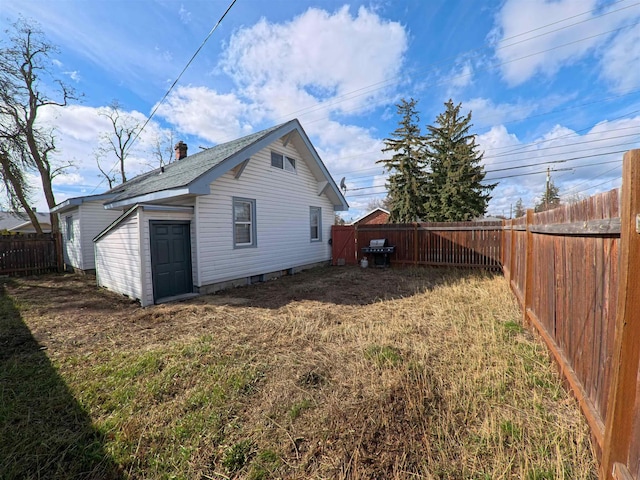 back of house with a yard, an outbuilding, a fenced backyard, and roof with shingles