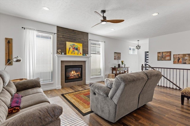 living area with a wealth of natural light, a tiled fireplace, ceiling fan, and wood finished floors