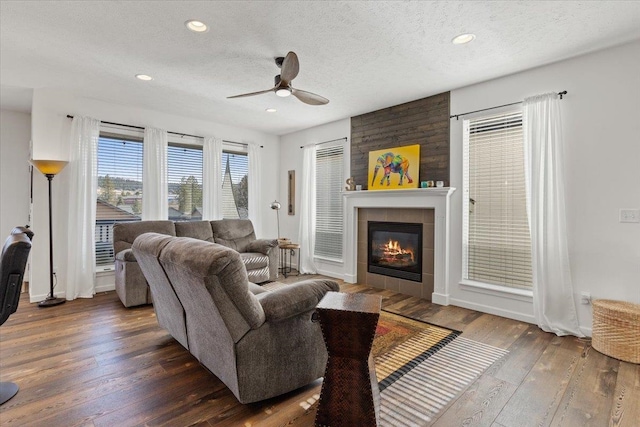 living room featuring hardwood / wood-style floors, a ceiling fan, recessed lighting, a tile fireplace, and a textured ceiling