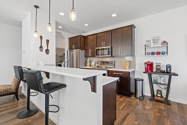 kitchen featuring backsplash, stainless steel appliances, dark brown cabinetry, a breakfast bar area, and light countertops