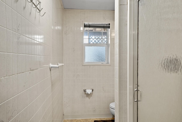 full bathroom featuring a shower with door, toilet, and tile walls