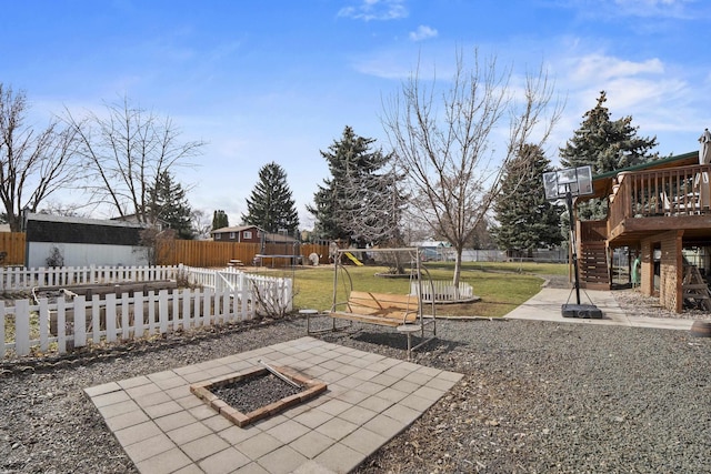 view of yard with a deck, a trampoline, a fenced backyard, a playground, and a fire pit