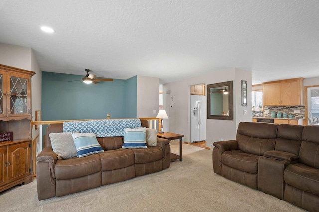 living area with light colored carpet, a ceiling fan, and a textured ceiling