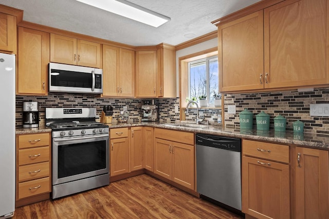 kitchen with dark stone counters, decorative backsplash, appliances with stainless steel finishes, wood finished floors, and a sink