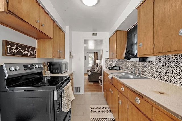 kitchen featuring electric stove, a sink, backsplash, black microwave, and light countertops