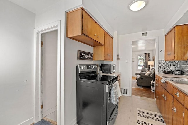 kitchen with backsplash, light countertops, light tile patterned floors, brown cabinets, and range with electric stovetop