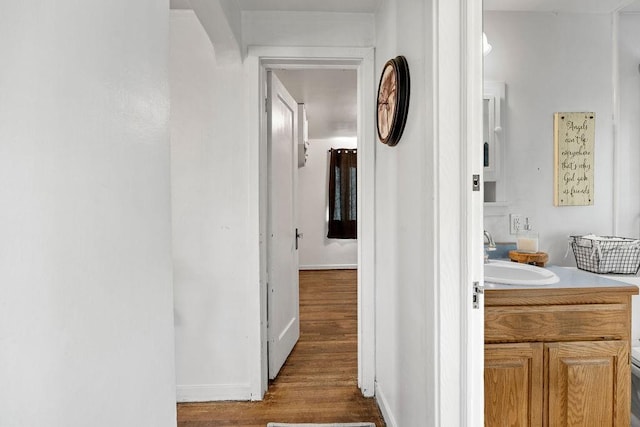 hall featuring wood finished floors, baseboards, and a sink