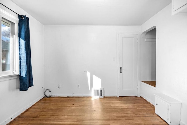 spare room featuring arched walkways, baseboards, and wood finished floors