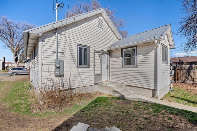 rear view of property featuring entry steps, metal roof, and fence