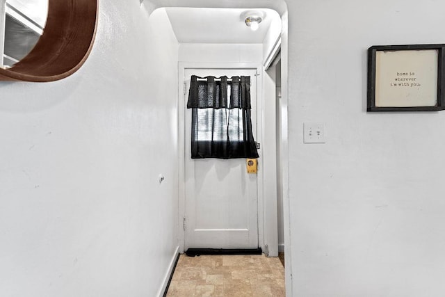 hallway featuring stone finish flooring and baseboards